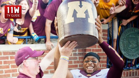 27 September 2014: Minnesota head coach Jerry Kill, left, and defensive back Cedric Thompson (2) lift up and celebrate with the Little Brown Jug trophy, after an NCAA college football game between the Michigan Wolverines and Minnesota, at Michigan Stadium in Ann Arbor, Michigan.