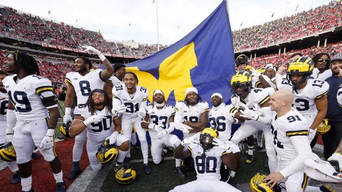 Michigan football players celebrate in front of their team flag at Ohio Stadium