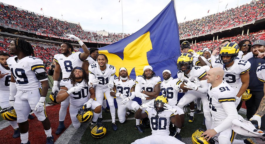 Michigan football players celebrate in front of their team flag at Ohio Stadium